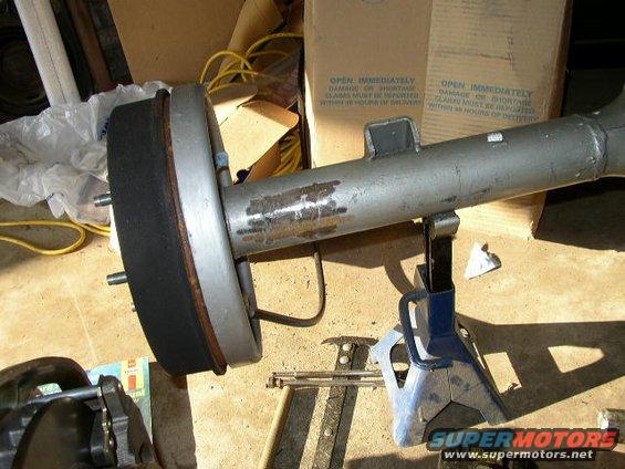 Rear axle assembly with brake drum on jack stands. Text on boxes reads "OPEN IMMEDIATELY"