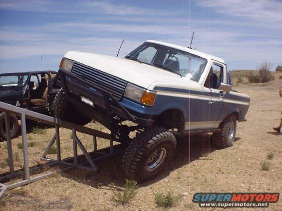 White and blue Ford pickup truck on a metal ramp, another vehicle to the left