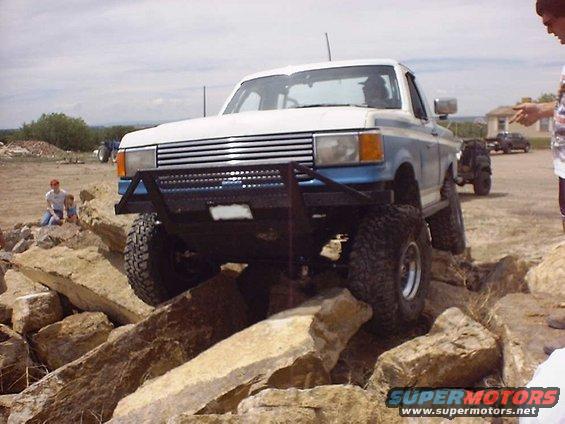 White and blue pickup truck with custom bumper navigating rocks