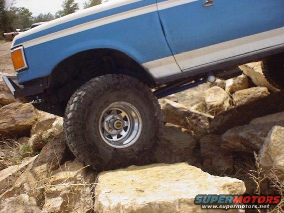 Blue and white Ford Bronco on rocks, front wheel visible, side view
