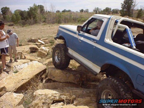 1988 Ford Bronco climbing over rocks on a trail, driver visible inside