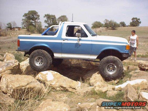 Blue and white 1987 Ford Bronco with lifted suspension navigating rocky terrain
