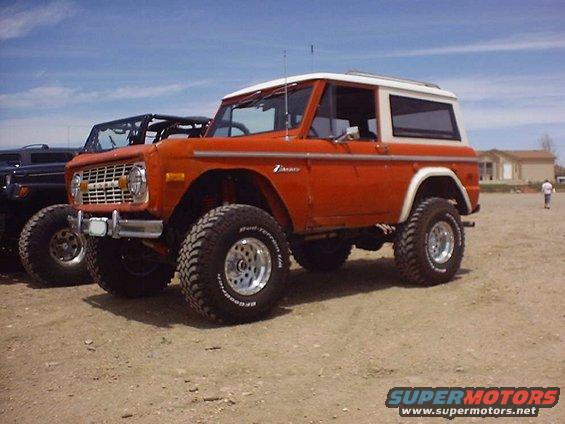 Orange Ford Bronco with white top, parked next to a black SUV. Off-road tires visible