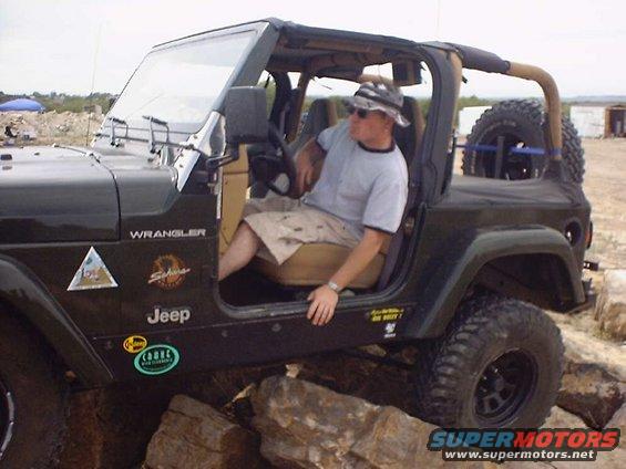 Man in hat sits in a dark green Jeep Wrangler parked on rocks