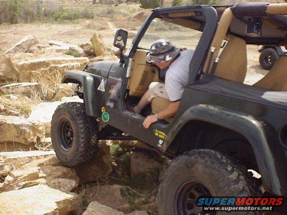 Green Jeep Wrangler on rocky terrain, driver entering. Another Jeep visible in background