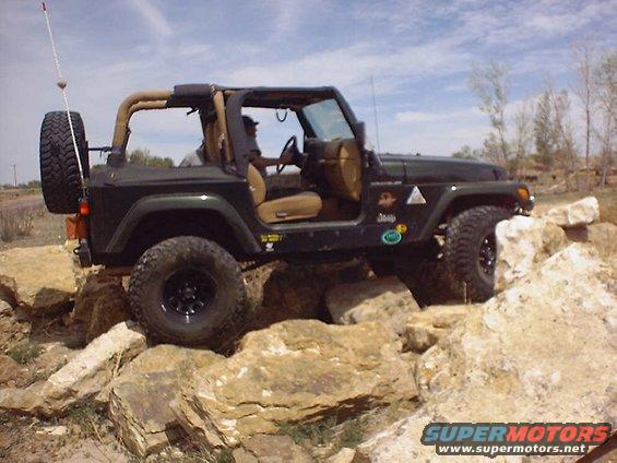 Dark green Jeep Wrangler with tan top navigating rocky terrain
