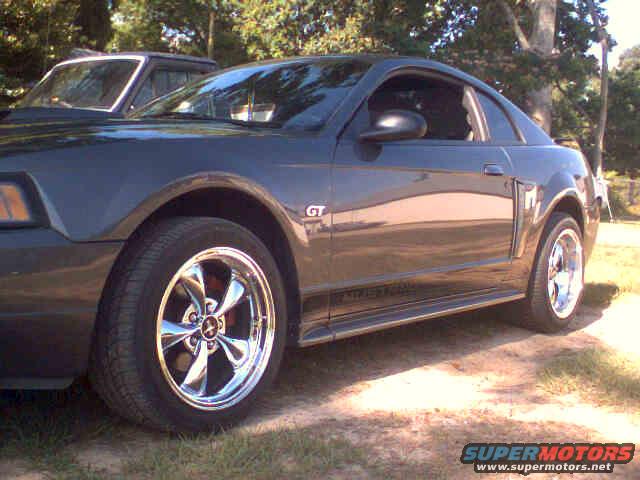 Dark gray 2003 Ford Mustang GT coupe with chrome wheels, parked outdoors. Another vehicle is partially visible behind it