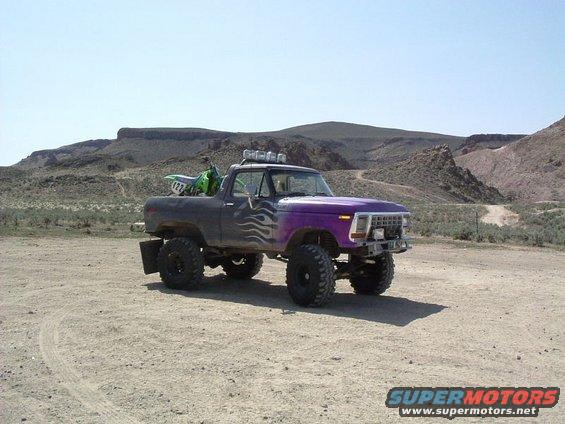 Lifted pickup truck, purple front end, flame decals, dirt bike in bed, desert background