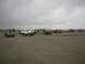 1978 Ford Bronco - A group of off-road vehicles gathered on a sandy beach, with people standing near some of them.