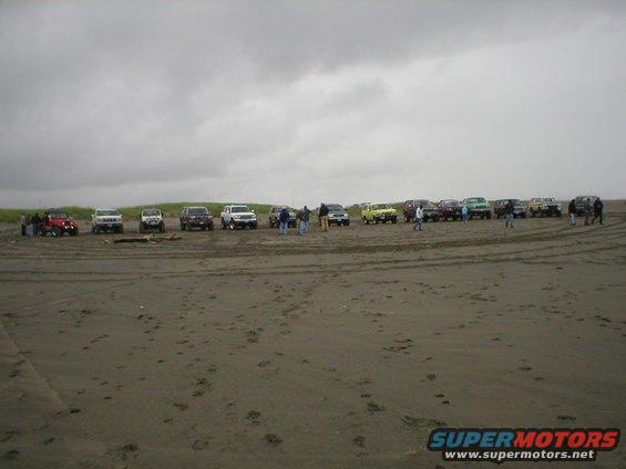 Group of SUVs and a red Jeep parked on a sandy beach under an overcast sky
