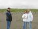 1978 Ford Bronco - Three people pose for a photo on a sandy beach with dunes and overcast skies in the background.