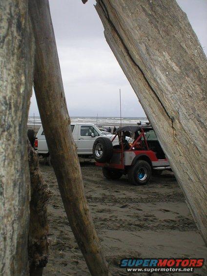 Two off-road vehicles parked on a sandy beach with driftwood in the foreground