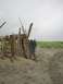 1978 Ford Bronco - Two people stand near a crude shelter made of driftwood on a cloudy beach.
