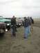 1978 Ford Bronco - Several trucks are parked on a beach as a group of men stand around.