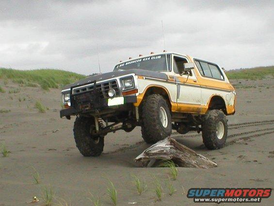 White and yellow 1978 Ford Bronco lifted on beach with "BIG BRONCOS 4X4 CLUB" sticker