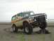 1978 Ford Bronco - A 1978 Ford Bronco navigates a sandy beach with its tires on a piece of driftwood.