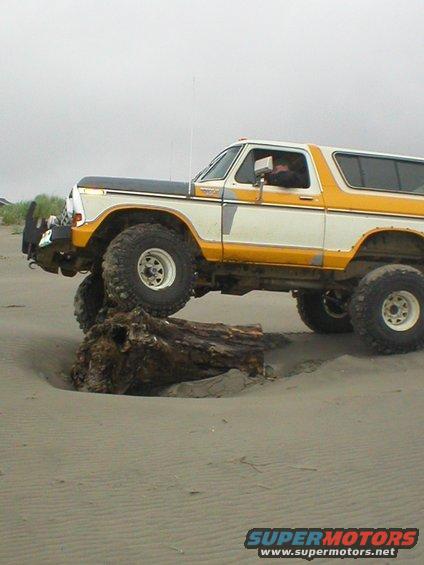 Ford Bronco driving over a large log on a sandy beach