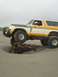1978 Ford Bronco - A lifted Ford Bronco navigates a sandy beach, with its front tire resting on a large piece of driftwood.