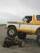 1978 Ford Bronco - A driver navigates a lifted Ford Bronco over a large log on a sandy beach under an overcast sky.