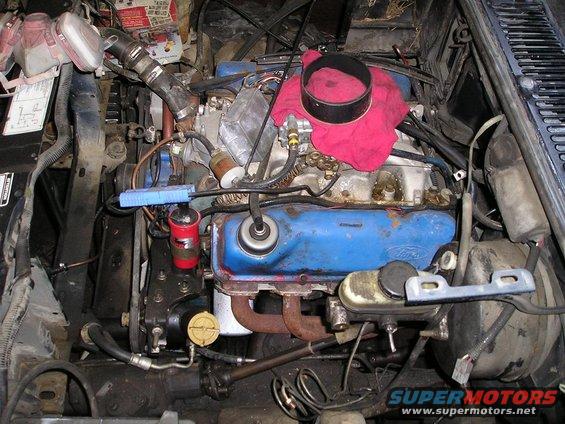 Engine bay with blue Ford engine, red ignition coil, and oil filter. A red cloth is draped over part of the engine
