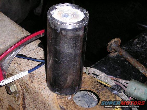 Close-up of a welded metal cylinder attached to a rusty vehicle frame with wiring nearby