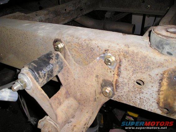 Close-up of a rusted vehicle frame section with new bolts and a black component labeled 'CANADA'