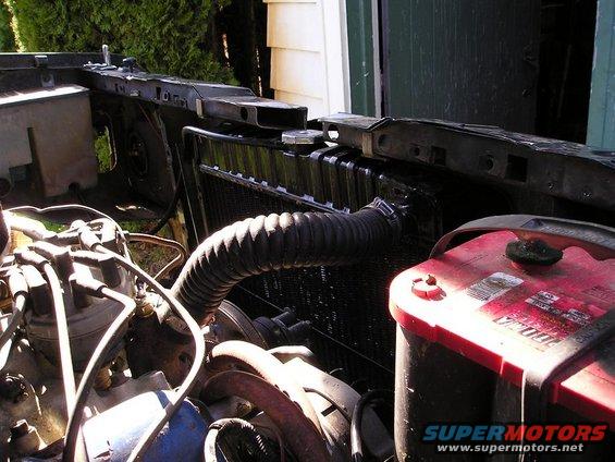 Engine bay showing radiator, hoses, and a red battery. Some wiring is visible