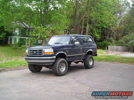 Dark blue 1994 Ford Bronco parked on asphalt with trees and a house in the background