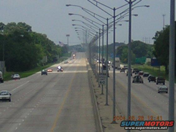 Highway scene with multiple vehicles, streetlights, and trees under a cloudy sky