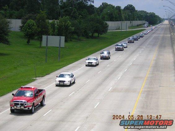 Funeral procession on highway with multiple cars and a red pickup truck in the foreground