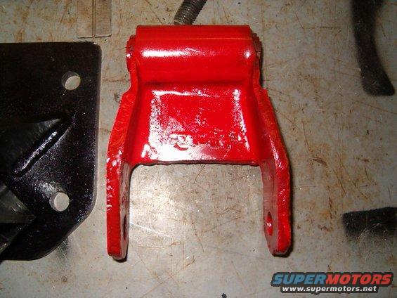 Red painted metal bracket next to a black metal bracket on a workbench