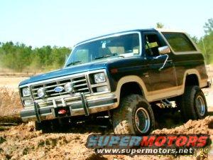 Blue 1985 Ford Bronco with lifted suspension driving on dirt