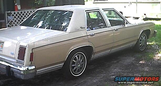Tan 1980s Ford Crown Victoria sedan, rear quarter view, with chrome trim and whitewall tires