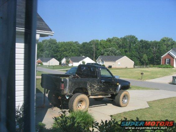 Black pickup truck with lifted suspension and large tires, covered in mud, parked on a driveway