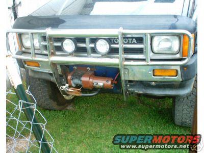 Front of a dark-colored Toyota truck with a chrome grille guard, two fog lights, and a winch mounted below the grille