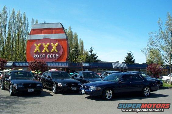 Dark sedans parked in front of XXX Root Beer building, one is a 2000 Ford Crown Victoria
