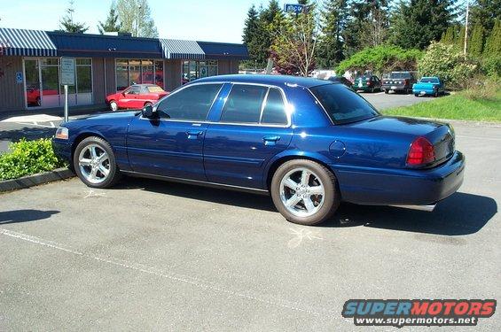 Blue sedan parked in a lot, side view. The car has tinted windows and aftermarket wheels