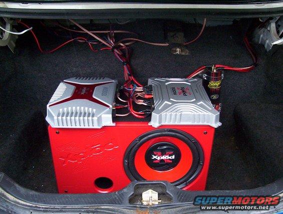 Car trunk interior showing two amplifiers and a red subwoofer with 'Xplod' branding