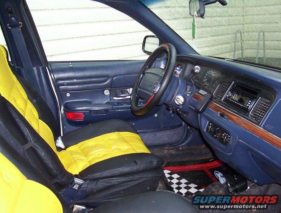 Interior view of a car with blue dashboard and yellow and black seat covers. Steering wheel and radio visible