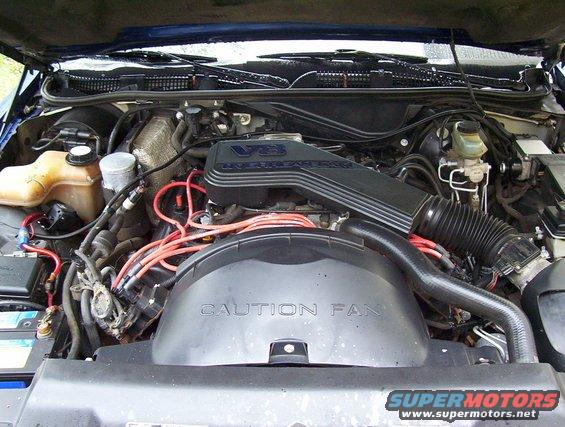 Blue Ford Crown Victoria engine bay with V8 engine cover and "CAUTION FAN" shroud