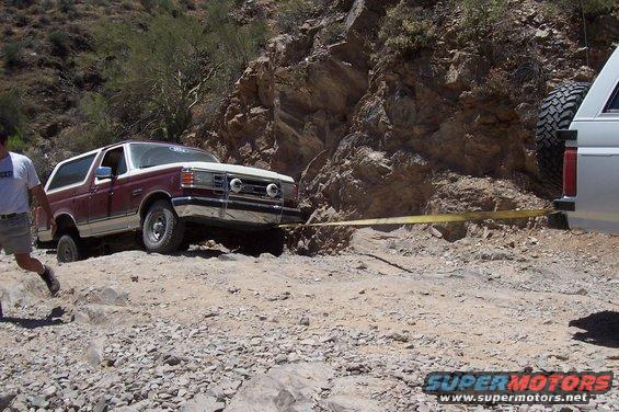 Maroon and white Ford Bronco stuck on a rocky trail, being pulled by another vehicle