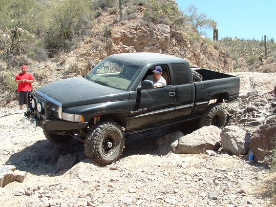 Black Dodge Ram pickup truck with off-road tires navigating rocky trail. Driver visible