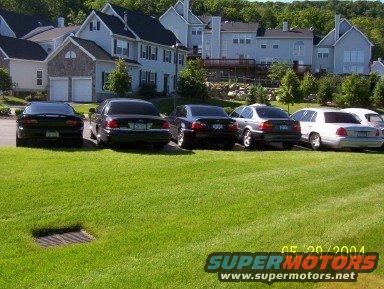 Several cars parked on grass in front of houses. One looks like a Crown Victoria