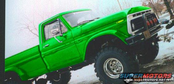 Green pickup truck with large tires and a chrome grille, viewed from a low angle