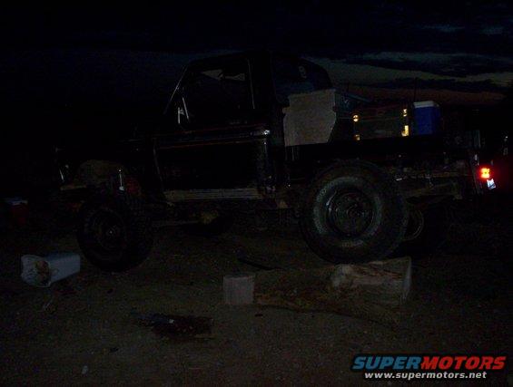 Black 1978 Ford Bronco on a log, side view, dark sky