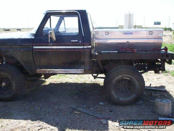 Side view of a black flatbed truck with a toolbox and off-road tires