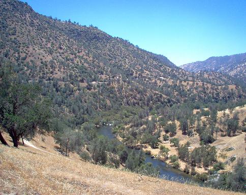 Dry hills covered in trees and brush surround a winding river in a valley under a clear blue sky