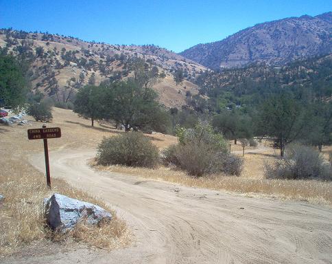 Dirt road curves through dry hills with a sign reading "CHINA GARDENS 4WD ROAD"