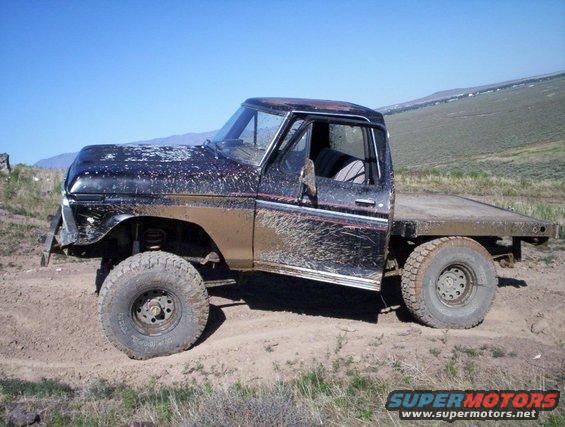 Mud-splattered black Ford F-Series flatbed truck with a lifted suspension and off-road tires, parked on a dirt track