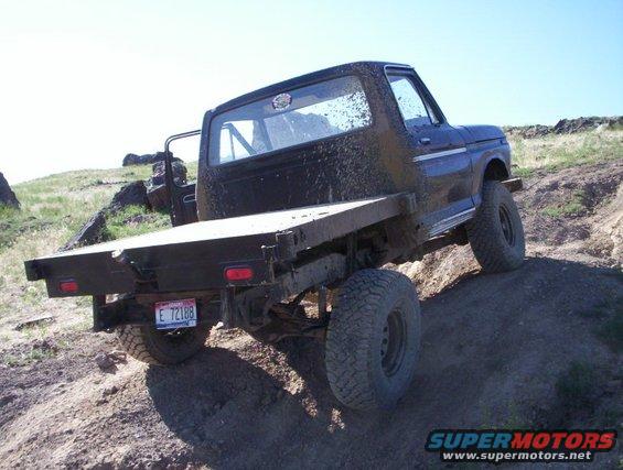 Ford flatbed truck driving off-road, mud splattered on body. License plate E 72188